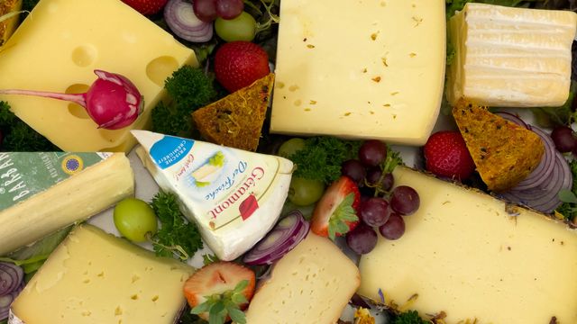 A top-down photograph of a variety of cheeses, grapes and other fruits. 
