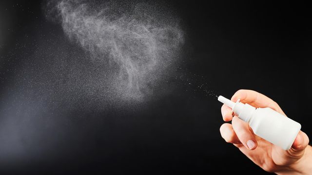 Human hand holding a white nasal spray bottle. A mist of white droplets has been sprayed into the air.  