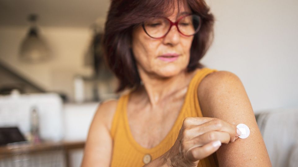 Middle-aged woman applying a patch to her arm, representing hormone therapy for menopause.