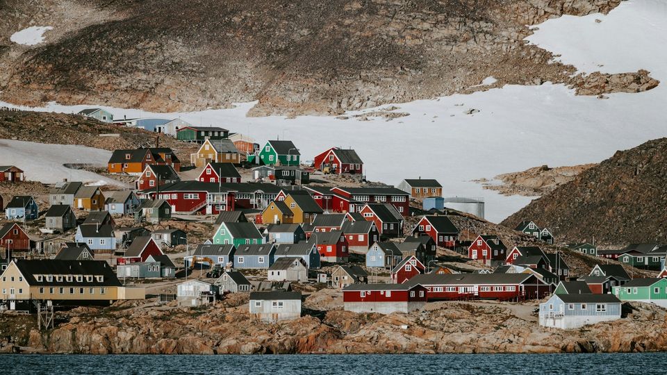 Colorful houses along a rocky Greenland coastal village with ice visible in the background.