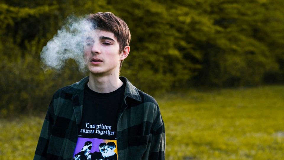 Teen exhaling vapor from an e-cigarette outdoors, highlighting youth vaping and e-cigarette use.