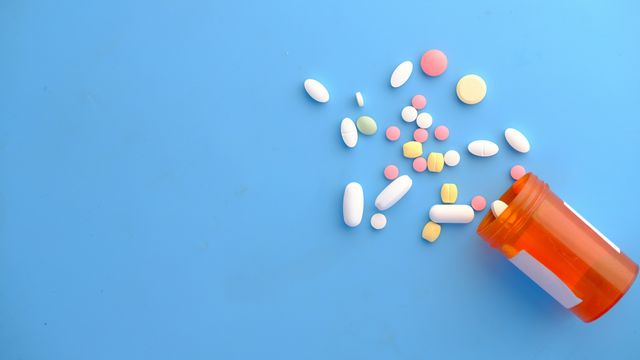 Tipped over orange medication bottle, with assortment of pills scattered over blue surface. 