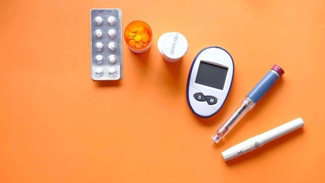 Blood glucose meter, insulin pen, and diabetes medication on an orange background. 