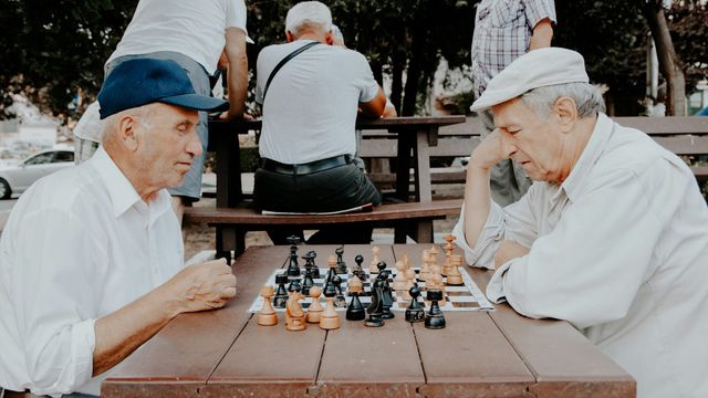 Two elderly men playing chess in a park, symbolizing genetics of aging and cognitive health. 
