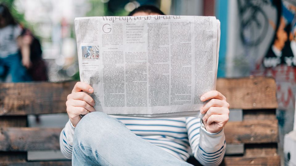 A person reading a newspaper, holding it in front of their face.