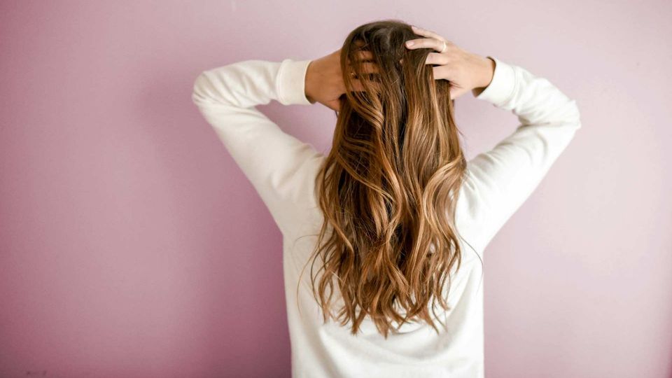 Woman in a white jumper holding her hair against a pink background.