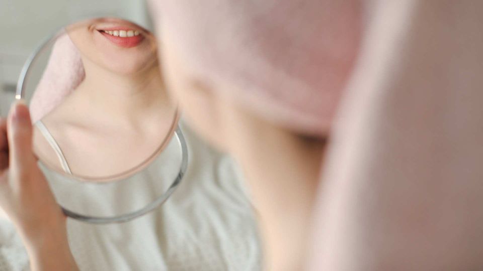 Girl holding a mirror showing clear skin, illustrating genetic skin disease awareness.