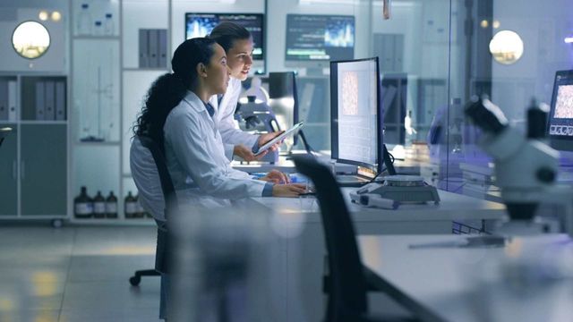 Researchers analyzing data on computer screens in an automated laboratory environment. 