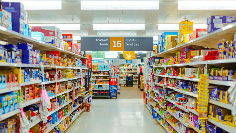A photo of a supermarket aisle, with the shelves containing a variety of processed chocolates, sweets and other snacks.