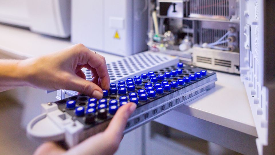 Technician loading vials into a mass spectrometer for proteomics analysis.