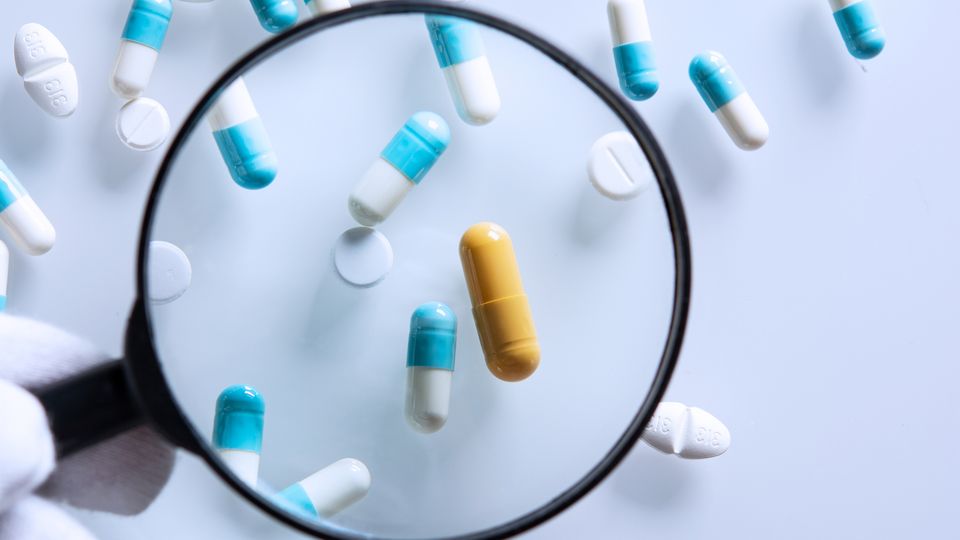 Magnifying glass looking over an assortment of pills laid out on a white surface.