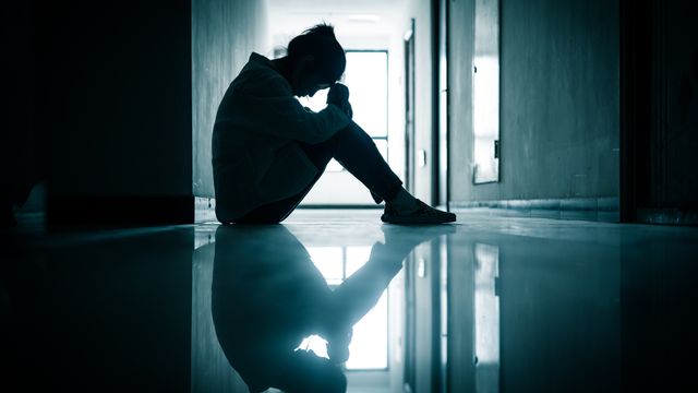 Silhouetted person sitting on the floor in a dim hallway, reflecting a moment of anxiety or distress. 