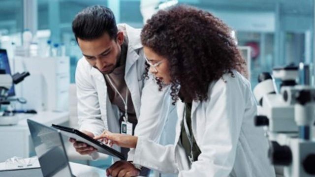 Researchers reviewing data on a tablet in a laboratory, illustrating cancer invasion research. 