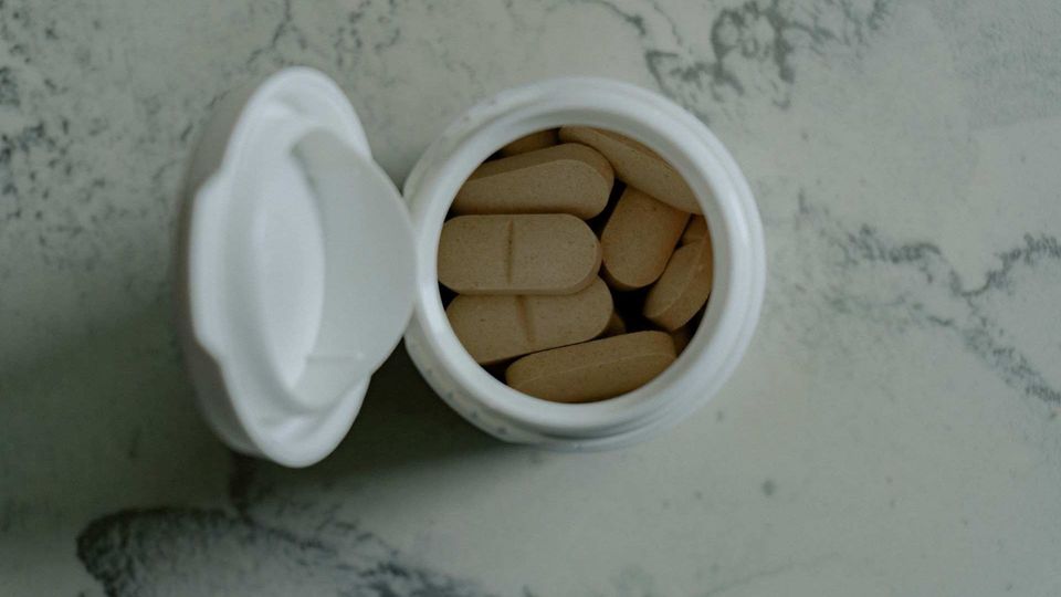 Birds-eye view of an open bottle of pills on a light stone surface.