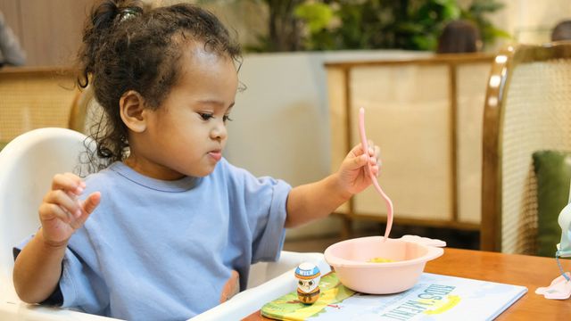 A young child eating puree from a pink plastic bowl. 