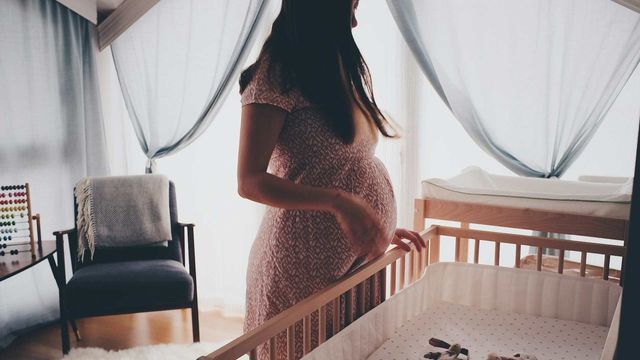 Pregnant woman standing beside a crib in a bright nursery room. 