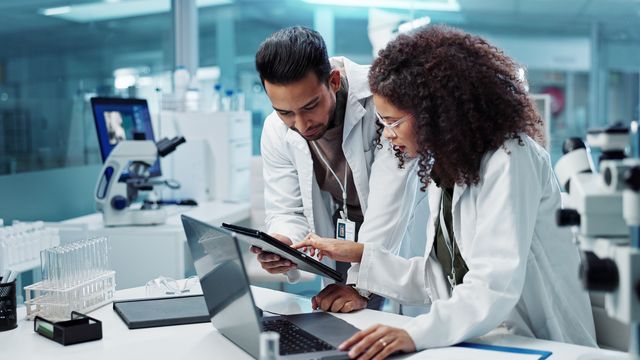 Two scientists in a lab reviewing data on a tablet and laptop, illustrating use of LIMS. 