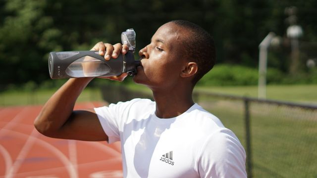 Man drinking water from a reusable bottle on an outdoor running track. 