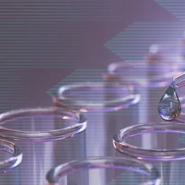 Several pink test tubes in a rack while a pipette drops liquid into one test tube