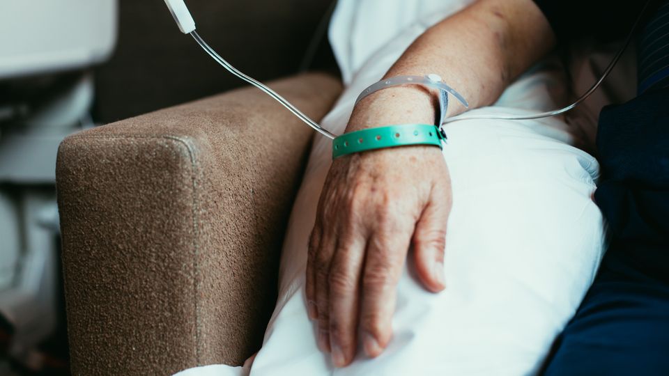 Arm of a man resting on a pillow, with a hospital wristband on and an intravenous drip by his side.