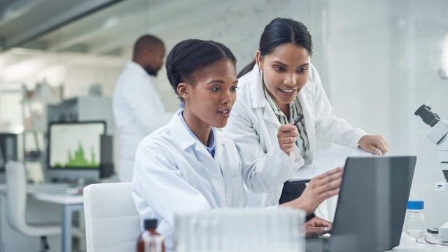 Scientists analyzing screen data on laptop in modern laboratory. 