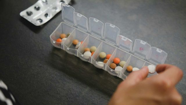 Weekly pill organizer with assorted medicines and tablets on a table. 