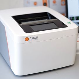 Axion BioSystems Maestro Pro instrument on lab bench beside computer displaying colorful data heatmap. 