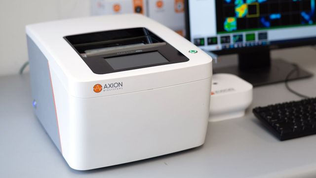 Axion BioSystems Maestro Pro instrument on lab bench beside computer displaying colorful data heatmap. 