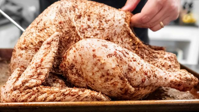 Raw turkey seasoned with spices on a roasting tray, ready for cooking. 