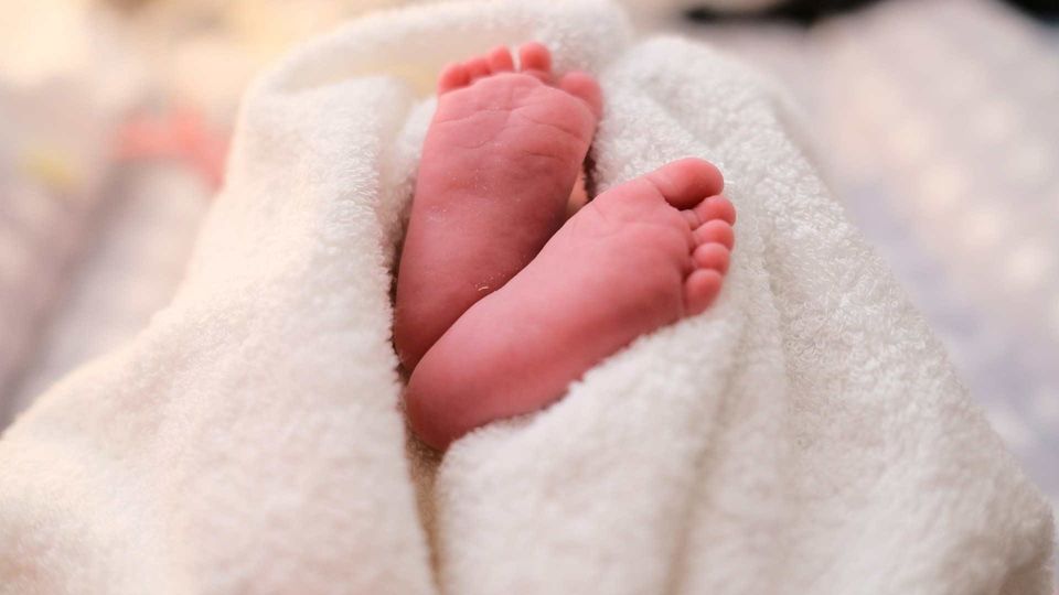 Baby feet wrapped in a soft white blanket, close-up newborn detail.