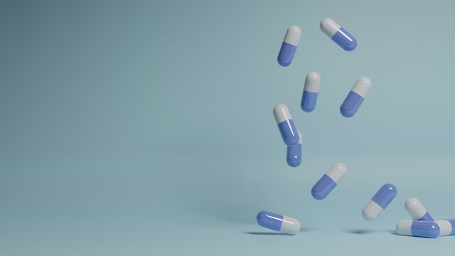 White and purple medication capsules pictured falling from a height against a pale blue background. 