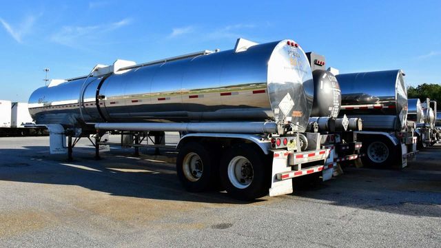 Stainless steel tank trucks parked in a lot for fuel or liquid transport. 