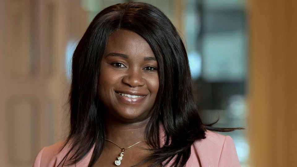 Headshot of Bamidele Farinre, smiling wearing a pink suit.