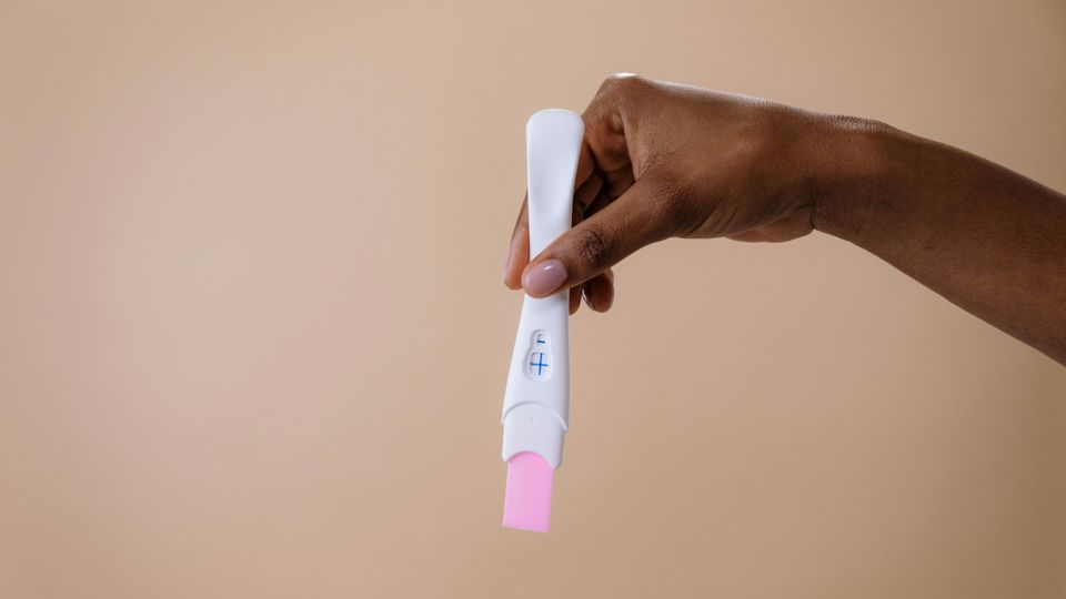 Hand of a woman holding a positive pregnancy test against a brown background.