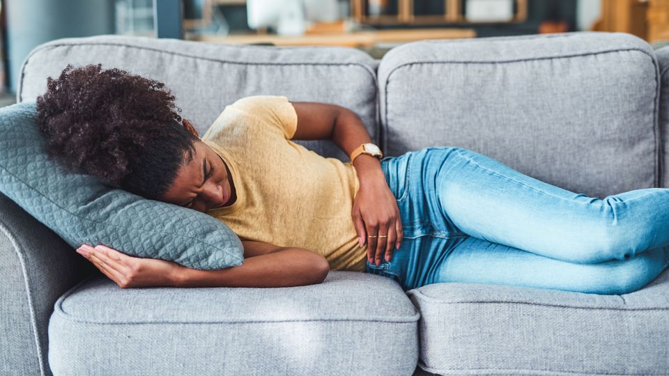 Woman lying on couch holding abdomen, illustrating chronic pain at home.