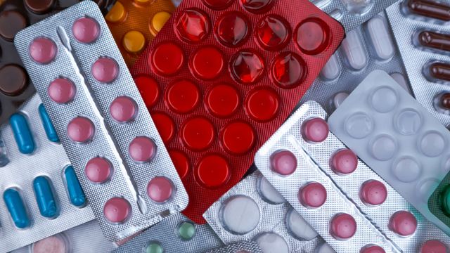 Assortment of medication blister packs, of different shapes and colours, piled on top of each other. 