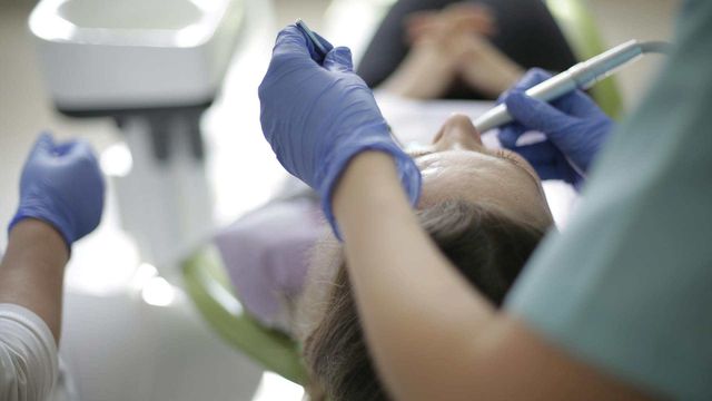 Dentist observing a patient’s mouth during a dental exam at a clinic. 