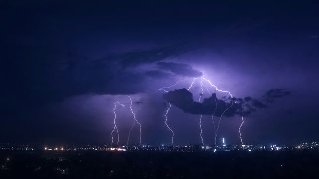 A large thunderstorm above a city. The lightning is illuminating the clouds with a purple color.  