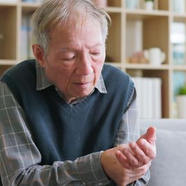 An elderly man with Parkinson's disease cradles his wrist. 