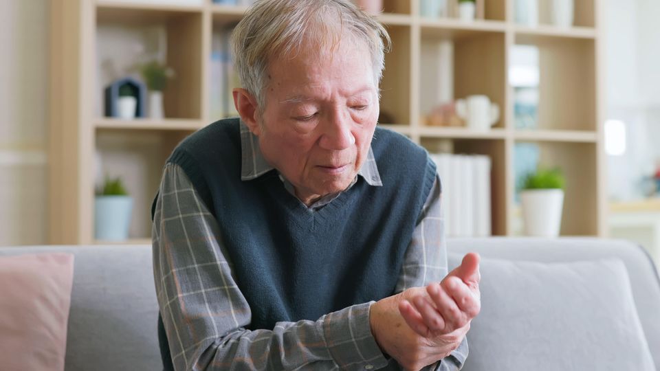 An elderly man with Parkinson's disease cradles his wrist.