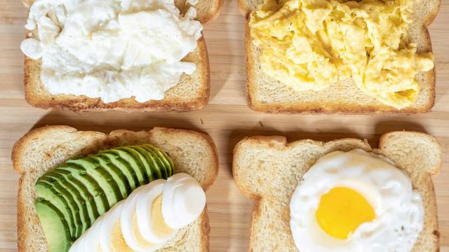 Four breakfast bread toasts topped with poached egg, scrambled eggs, fried egg, and avocado slices. 