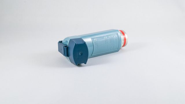 Asthma inhaler lying on a white surface, showing a blue metered-dose inhaler used for breathing treatment. 