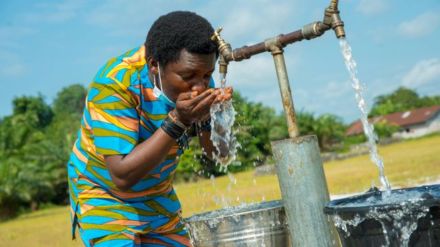 A man cupping his hands and drinking from a public water tap. 