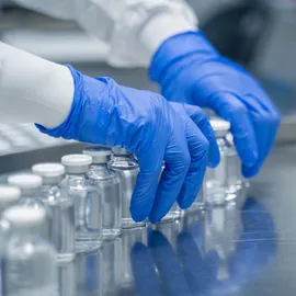 Technician with blue gloves arranging glass vials on a biopharma downstream processing line.