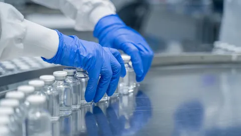 Technician with blue gloves arranging glass vials on a biopharma downstream processing line.