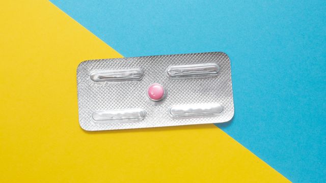 Birds-eye view of tablet sachet containing a single pink pill, placed on a blue and yellow surface. 