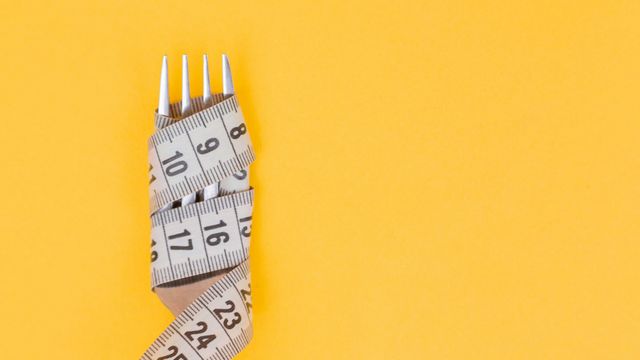 Birds-eye view of a measuring tape wrapped around a fork, laid on a yellow surface. 