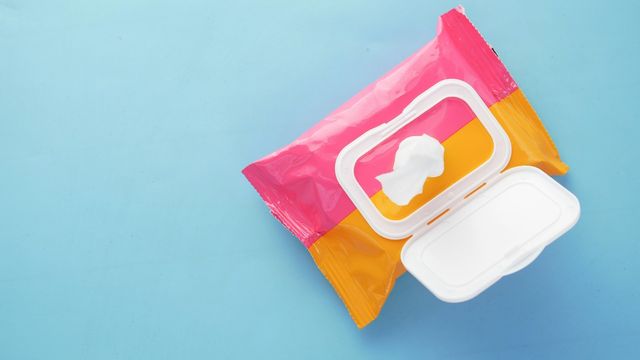 Colorful pack of wet wipes with an open lid and a single wipe on a blue background. 