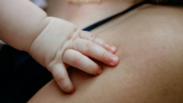 A baby's hand gently resting on a parent’s shoulder, showing skin-to-skin contact. 