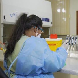 A lab worker in protective gear uses pipettes at a laboratory bench. 